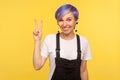 Portrait of happy cute hipster woman smiling and showing victory or peace gesture. yellow background, studio shot Royalty Free Stock Photo