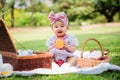 Portrait of a happy cute little Asian baby girl sitting smiling on lawn holding orange fruit with basket while relaxing picnic in Royalty Free Stock Photo