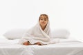 Portrait of happy, cute little baby-girl sitting on soft white bedding in towel after shower against white studio Royalty Free Stock Photo