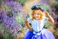 Portrait of happy cute little blonde curly girl wearing lavender dress and wreath in lavender field with violet flowers around in Royalty Free Stock Photo