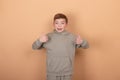 Portrait of happy cute teenager boy in green clothes standing and showing thumb up gesture,  on brown background Royalty Free Stock Photo