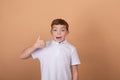 Portrait of happy cute teenager boy in white T-shirt standing and showing thumb up gesture,  on brown background Royalty Free Stock Photo