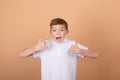 Portrait of happy cute teenager boy in white T-shirt standing and showing thumb up gesture,  on brown background Royalty Free Stock Photo