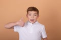 Portrait of happy cute teenager boy in white T-shirt standing and showing thumb up gesture,  on brown background Royalty Free Stock Photo