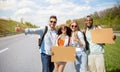 Portrait of happy diverse friends hitchhiking together on highway, making thumb up gestures, holding empty signs Royalty Free Stock Photo