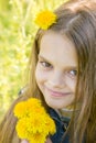 Portrait of happy eight year old girl with dandelions in hands, against a background of green foliage