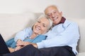 Portrait of happy elderly man with arm around spouse lying on sofa at home Royalty Free Stock Photo