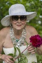 Portrait of a happy elderly woman 65 - 70 years old in a white straw hat with red peony flower, closeup Royalty Free Stock Photo