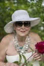 Portrait of a happy elderly woman 65 - 70 years old in a white straw hat with red peony flower, closeup Royalty Free Stock Photo