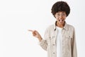 Portrait of happy emotive and expressive young dark-skinned woman in beige trendy shirt and glasses pointing left with