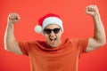Portrait of happy and excited man in santa hat, rejoicing and winning something, celebrating new year, standing over red