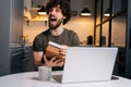 Portrait of happy excited young bearded man opening gift box with present during video call on laptop computer sitting Royalty Free Stock Photo