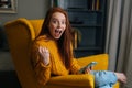 Portrait of happy excited young woman holding smartphone and smiling looking at camera sitting in yellow armchair Royalty Free Stock Photo