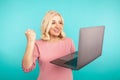 Portrait of happy exited abult lady with laptop isolated over the blue studio.