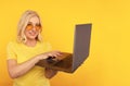 Portrait of happy exited abult lady with laptop isolated over the yellow studio.