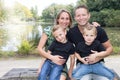 Portrait of happy family of four in a green summer park lake pond side