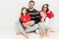 Portrait of happy family of four members: attractive brunette woman, her husband and two small daughters sit on floor, isolated o Royalty Free Stock Photo