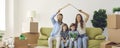 Portrait of happy family with kids sitting at home on sofa holding cardboard roof over their heads.