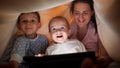 Portrait of happy family playing with tablet computer in tent made of bedsheets and blankets. Family having time together, Royalty Free Stock Photo