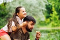 Portrait of happy family sitting on picnic in park forest around trees bushes. Little daughter sitting on fathers back.