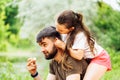 Portrait of happy family sitting on picnic in park forest around trees bushes. Little daughter sitting on fathers back.