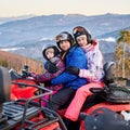 Happy family of three spending great time together in the mountains in winter riding quad bike