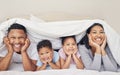 Portrait of happy family with two children lying under duvet smiling and looking at camera. Little girl and boy lying in Royalty Free Stock Photo