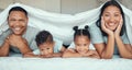 Portrait of happy family with two children lying under duvet smiling and looking at camera. Little girl and boy lying in Royalty Free Stock Photo