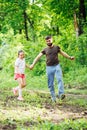 Portrait of happy family walking in park. Little cheerful daughter holding hand of middle-aged smiling bearded father. Royalty Free Stock Photo