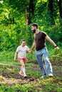 Portrait of happy family walking in park forest around trees, having fun. Little daughter keeping tight hold of father. Royalty Free Stock Photo