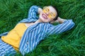 Portrait of Happy fancy young woman with short hair in casual blue striped suit, yellow shirt, glasses lying down on green grass, Royalty Free Stock Photo