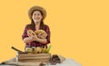 Portrait of happy farmer woman standing holding fresh cacao fruit and looking at camera with isolated on yellow background Royalty Free Stock Photo