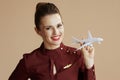 Portrait of happy female air hostess isolated on beige background with a little airplane