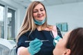 Portrait of happy female dentist in mask sitting, holding dentist tools, smiling and examining young woman in dental chair, Royalty Free Stock Photo