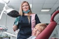 Portrait of happy female dentist in mask standing, holding dentist tools, smiling and examining young boy in dental chair, healthy Royalty Free Stock Photo