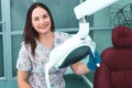 Portrait of happy female dentist sitting in the dental chair, holding lamp, smiling at the camera and ready to accept a new