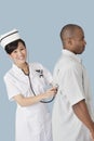 Portrait of a happy female doctor examining male patient's back with stethoscope over light blue background