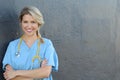 Portrait of happy female nurse with stethoscope standing arms crossed isolated over dark gray background Royalty Free Stock Photo