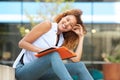 Happy female student laughing outside with pen and book