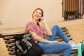 Happy female traveler sitting with bags and talking on cell phone Royalty Free Stock Photo