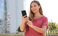 Portrait of happy friendly young woman using her mobile phone outdoors in a modern urban street Royalty Free Stock Photo