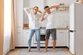 Portrait of happy funny family dancing in kitchen at home, making v sign gesture near eyes, smiling, celebrating completion of the Royalty Free Stock Photo
