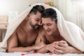 Portrait of a happy gay couple lying under a blanket on the bed together Royalty Free Stock Photo