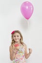 Portrait of happy girl holding cupcake and party balloon over colored background Royalty Free Stock Photo