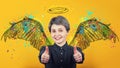 Portrait of happy girl keeps thumbs up over yellow background, smiling broadly imagining herself an angel with fluffy wings behind Royalty Free Stock Photo