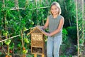 Portrait of happy girl next to hotel for insects in of wooden birdhouse in garden