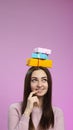 Portrait of a happy girl a pile of gift boxes on her head,smiling young woman imagines with a finger near the mouth presents,