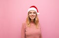 Portrait of happy girl in a santa hat on a pink background, looking away and smiling. Christmas lady in cute happy clothes