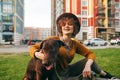 Portrait of happy girl sitting on lawn with dog, stroking puppy and smiling. Cute lady in a hat relaxing on the grass in the yard Royalty Free Stock Photo