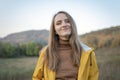 Portrait of happy girl in yellow jacket on mountainous area background. Young woman walks in nature on autumn day Royalty Free Stock Photo